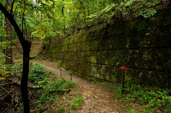 A mossy stone wall lines a paved dirt pathway through the woods.