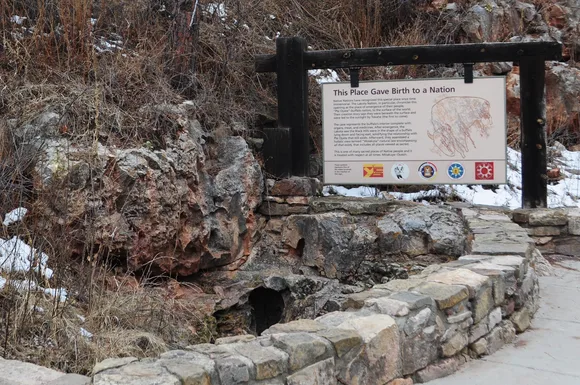 a small hole in a stone depression next to a large sign and short rock wall