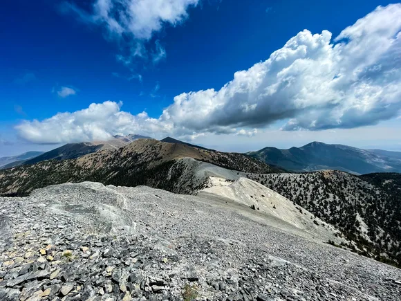 a bare alpine ridge with blue sky and white puffy clouds above.